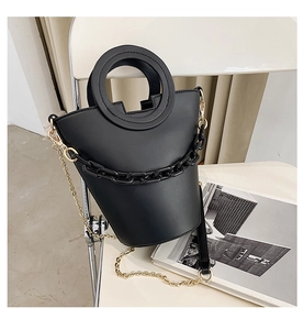 Detail of minimalist black PU leather bag with golden chain strap on a white chair