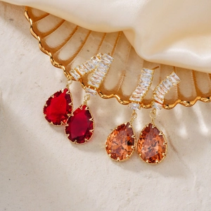 Detail of teardrop zircon earrings in deep red and champagne on a shell tray