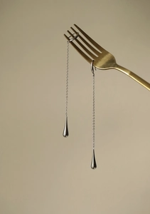Detail of silver long chain earrings with drop pendants hanging on a golden fork