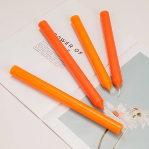Set of four orange taper candles with wicks on a decorative vintage book page