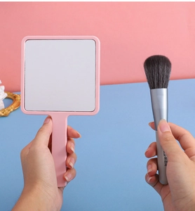Detailed close-up of pink handheld square makeup mirror with ergonomic plastic handle