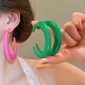 Close-up of bright green and pink C-shaped resin hoop earrings with high-gloss finish