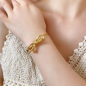 Dettaglio del bracciale in metallo dorato a forma di fiocco indossato su polso con pizzo