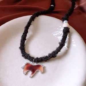 Close-up of woven rope necklace with wood beads and brown resin horse pendant in ceramic tray