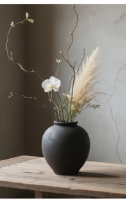 Vue détaillée du vase en céramique noir mat sur banc en bois avec fleurs décoratives