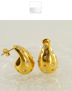 Macro shot of 18K gold teardrop earrings with embedded zircon crystals on a textured base