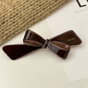 Close-up of a dark coffee bow hair clip with glossy mirror finish on a knit fabric