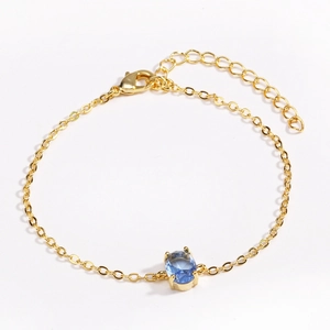 Detail of gold-plated chain bracelet featuring an oval blue crystal and lobster clasp
