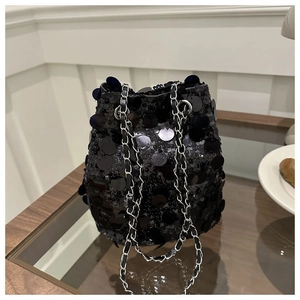 Elegante borsa a secchiello con paillettes nere e tracolla a catena su un tavolo