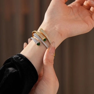 Detail of gold and silver plated bracelets with white zircons and green teardrop stones
