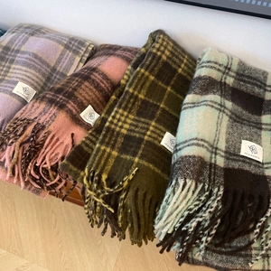 Detail shot of four retro plaid scarves with fringe tassels folded on a wooden bench
