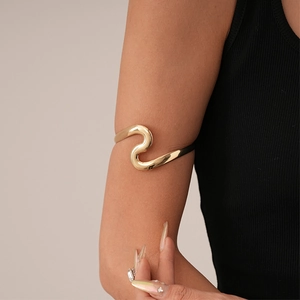 Close-up of stylish wavy gold metal upper arm cuff bracelet on female model