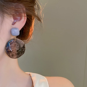 Close-up of irregular resin circle earrings with marble texture on female model