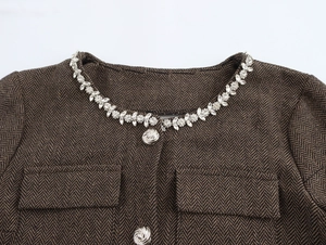 Détail de la veste en laine à chevrons avec chaîne strass et bouton rose argenté