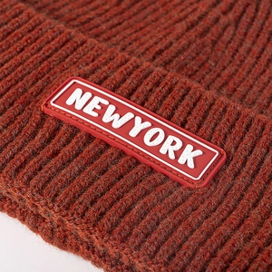 Close-up of rust red knit beanie featuring a New York rubber patch with ribbed texture