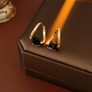 Elegant gold irregular square earrings with black gemstone on premium leather surface