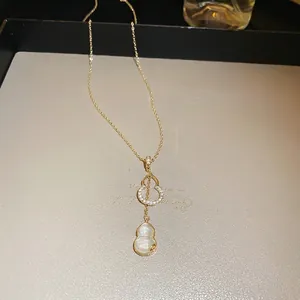 Détail d'un collier double épaisseur doré avec pendentif gourde et pierre blanche