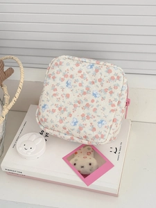 Trousse à maquillage matelassée à fleurs avec fermeture éclair rose sur un livre décoratif