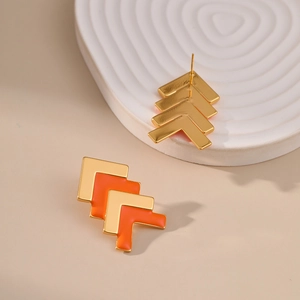 Macro view of gold V-shaped stud earrings with orange enamel on a textured tray