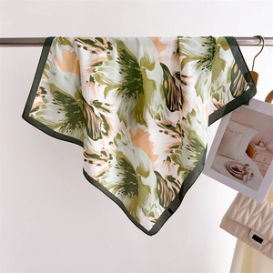 Floral print silk square scarf draped on a metal rod showing smooth texture and green border