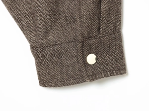 Detail of brown herringbone fabric jacket with a polished gold button on the cuff