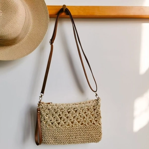 Beige hollow-out straw crossbody bag with brown leather strap hanging on a wooden hook