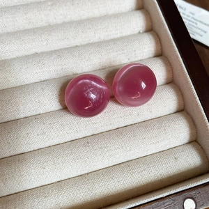 Macro view of round pink cat eye stone earrings displayed in a wooden jewelry box