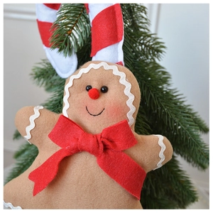 Detail of plush gingerbread man ornament with red bow on festive Christmas tree