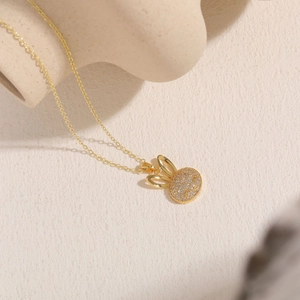 Macro shot of gold rabbit pendant with white zircon crystals on ivory texture background