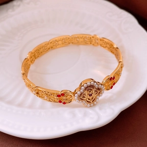 Detail of vintage hollow gold bangle with pearl clover and red zircon on white plate