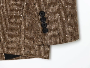 Macro shot of brown herringbone tweed blazer sleeve featuring four black resin buttons