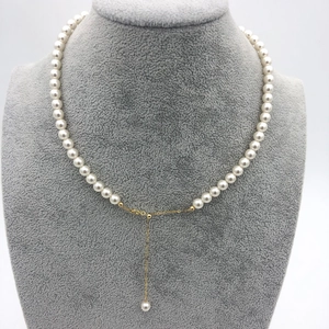 Close-up of white round pearl necklace with 14k gold adjustable chain on gray velvet stand