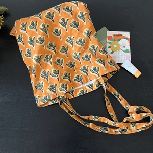 Flat lay of an orange canvas tote bag with green leaf prints and lifestyle accessories