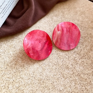 Detail of pink marble textured acrylic round earrings with silver glitter on beige surface