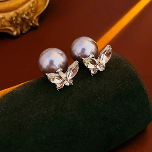 Gros plan de boucles d'oreilles papillon dorées avec perles mauves sur velours vert