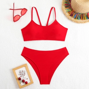 Flat lay of a red two-piece bikini set with sunglasses and a straw hat on a white texture