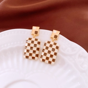 Macro shot of rectangular checkerboard enamel earrings on white textured porcelain