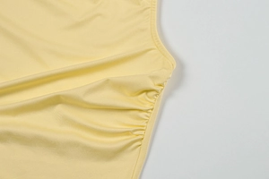 Detailed close-up of side ruching and pleated fabric on a pale yellow summer dress