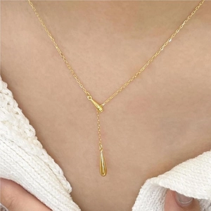 Detail of a minimalist gold teardrop pendant on a Y-shaped necklace worn by a model