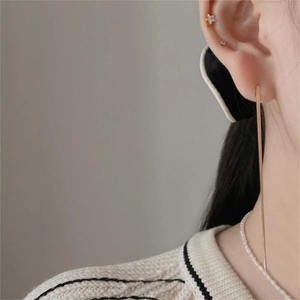 Detail of long gold drop chain earring styled with star stud and pearl necklace