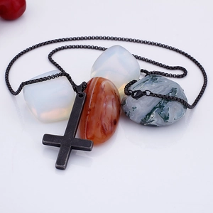 Close-up of black inverted cross necklace displayed on natural textured raw stones