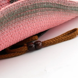 Macro detail of pink and green woven straw hat with wooden beads on a chin strap