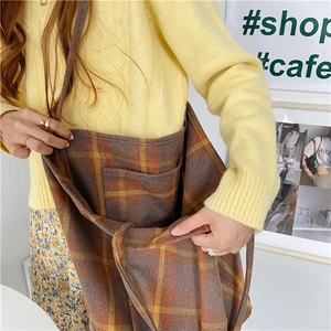 Close-up of a brown plaid woolen tote bag held by a model in a yellow sweater