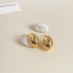 Close-up of polished 18K gold-plated oval stud earrings on a minimalist cream background
