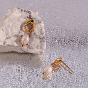Detail view of gold hoop earrings with white freshwater pearl and green gemstone accents