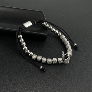 Detailed macro view of silver crown charm and textured beads on black braided men's bracelet