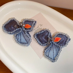 Detailed close-up of blue embroidered butterfly hair clip with crystal beads on a tray