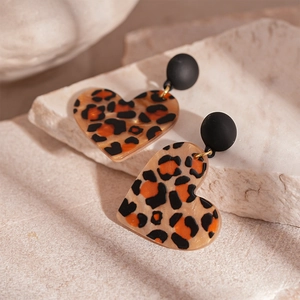 Detail of heart-shaped leopard print resin earrings with black circular studs on stone