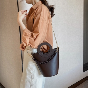Deep brown leather bucket bag with circular handle and bold front chain decoration