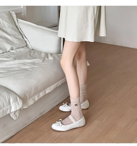 Detail of beige slouch socks with black bow embroidery paired with white Mary Jane shoes